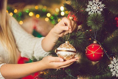 Closeup-toned-image-of-female-hand-putting-golden-bauble-on-Christmas-tree